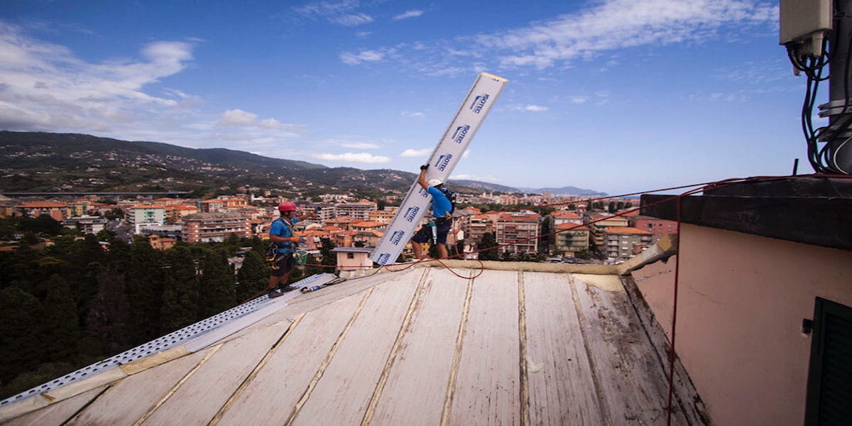 Un ouvrier de l'entreprise Acrobatica sur le toit, travaillant à l'installation de l'isolation thermique pour améliorer l'efficacité énergétique de la maison.