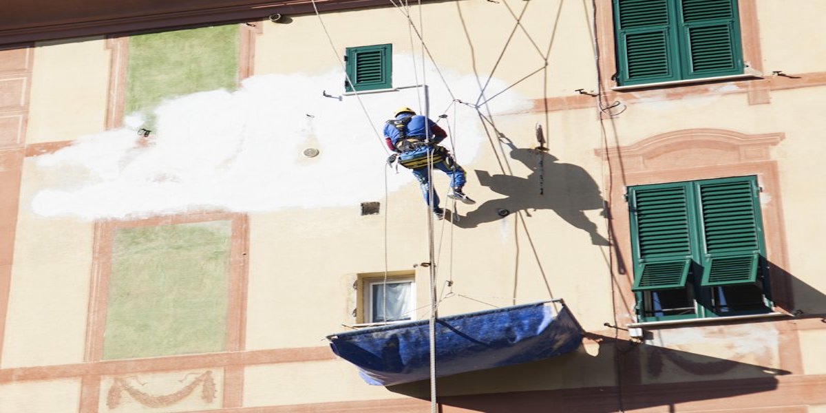 Un ouvrier de l'entreprise Acrobatica devant la façade en cours de rénovation, préparant l'installation de l'isolation thermique.