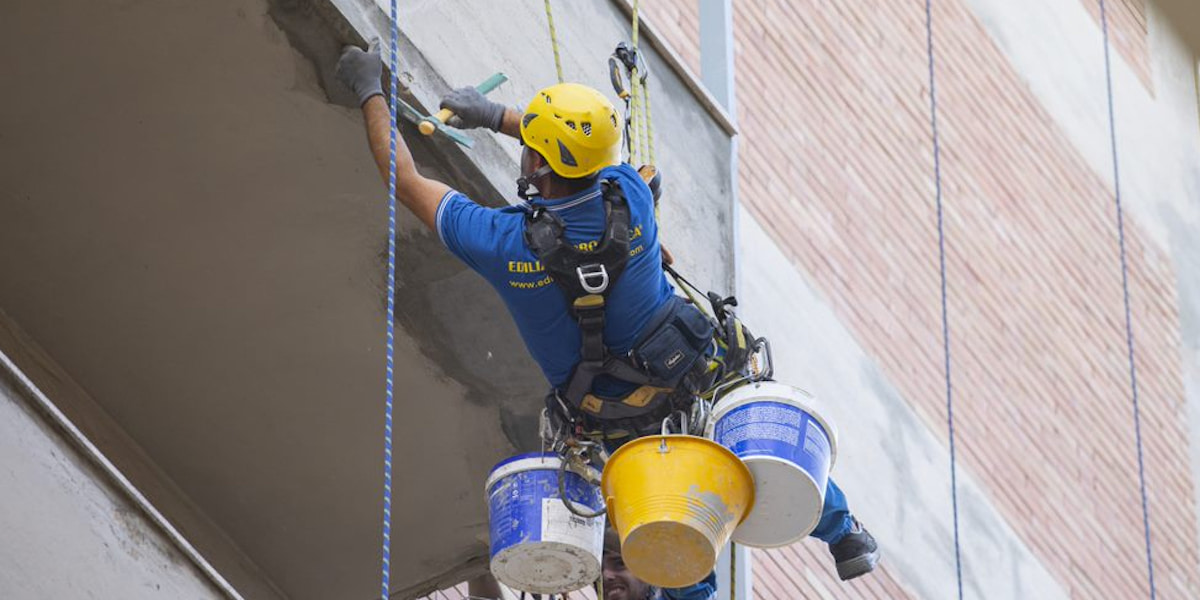 Ouvrier d'Acrobatica suspendu sur corde pour la fermeture terrasse en copropriété, vue depuis le bas.