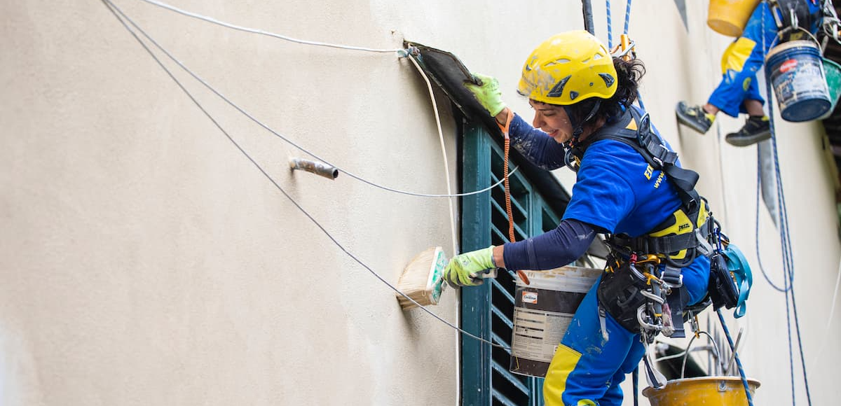 Ouvrière sur corde effectuant des travaux de rénovation énergétique sur une façade, bénéficiant du programme MaPrimeRénov' Rose.