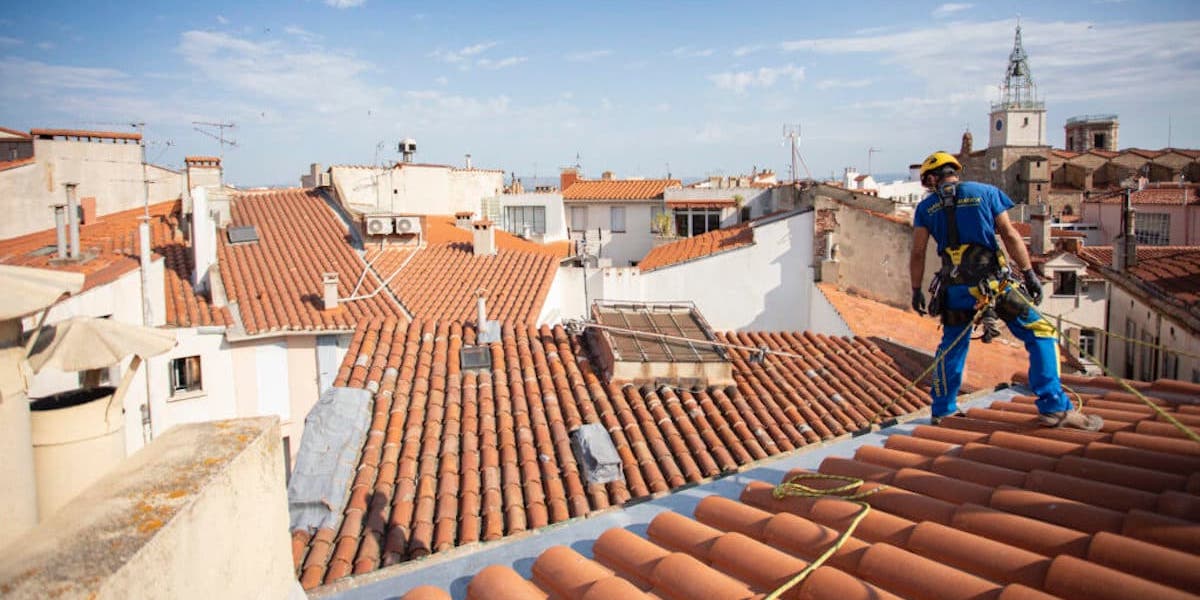 Ouvrier fixant des tuiles sur une toiture chaude pour assurer l'isolation thermique de la maison.