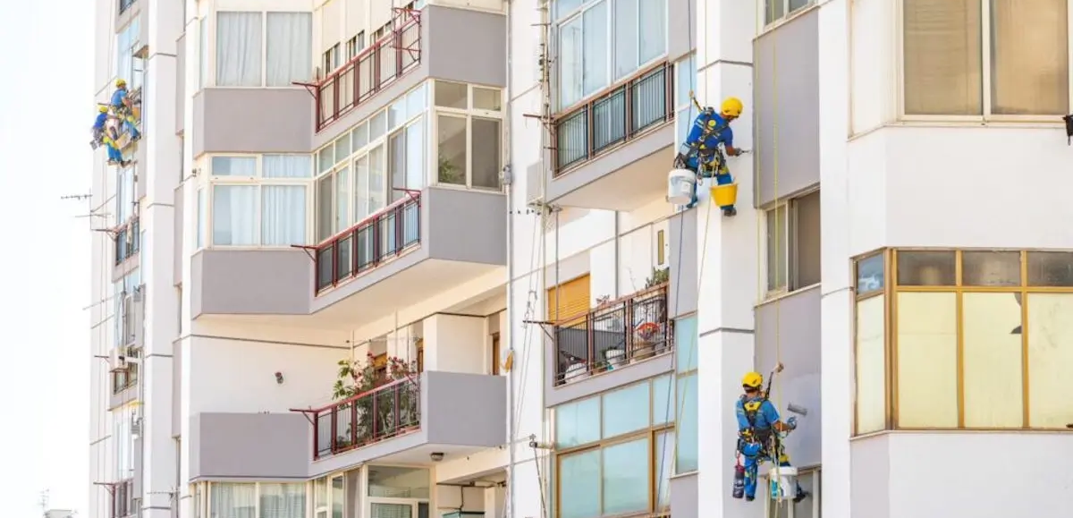 Plusieurs ouvriers Acrobatica sur corde travaillant à la rénovation d'un immeuble en copropriété.



