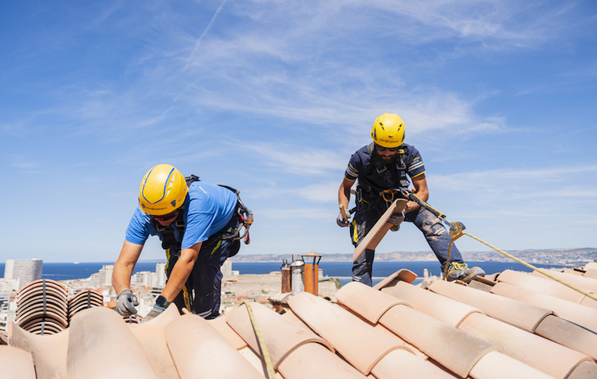 Deux techniciens cordistes en intervention sur un toit pour une rénovation énergétique sans échafaudage.