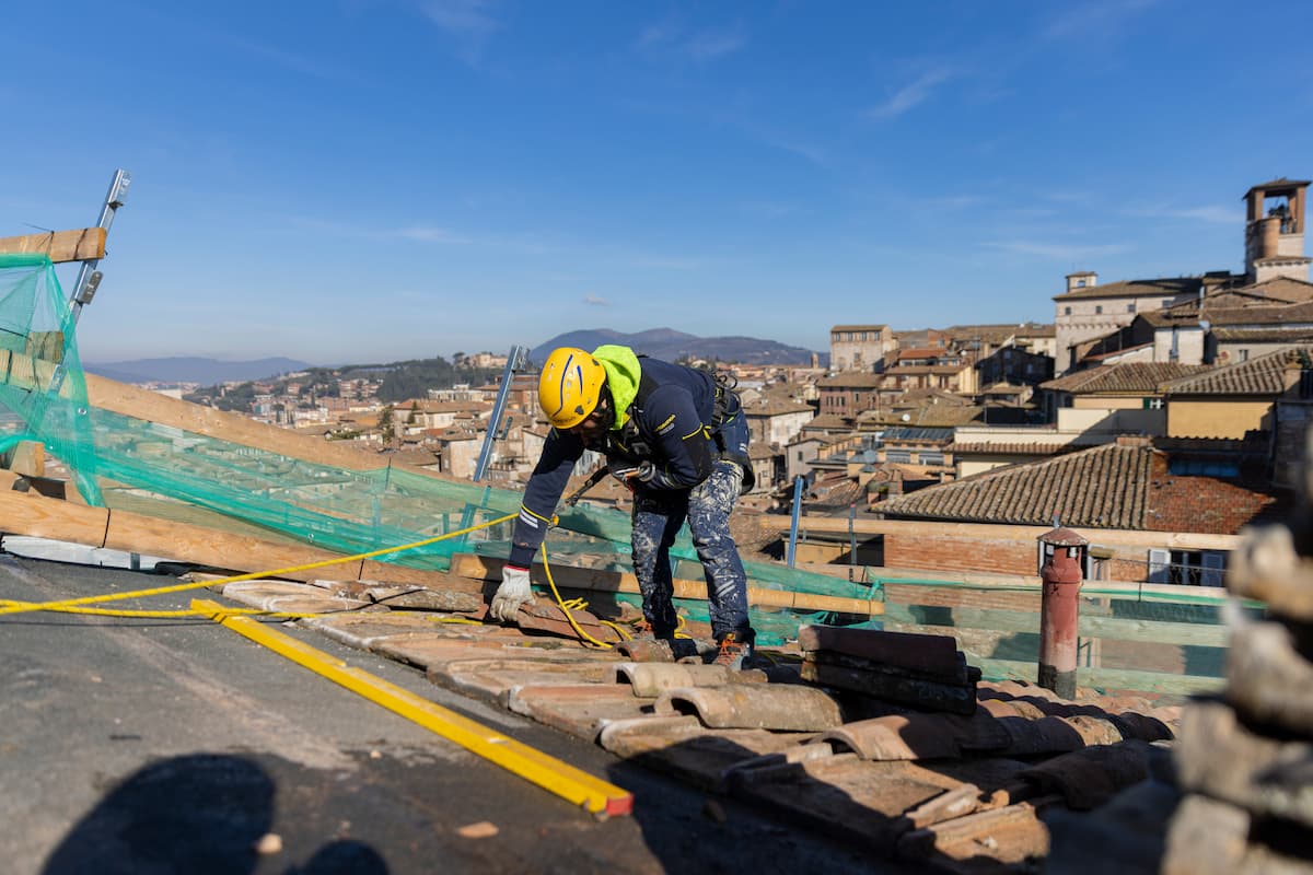 Ouvrier cordiste d'Acrobatica en train d'appliquer une membrane d'étanchéité bitumineuse sur la toiture-terrasse d'un immeuble.